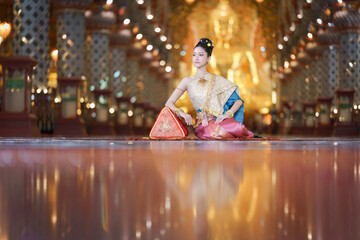 Elegant Thai pretty woman in traditional costume posing gracefully inside a golden temple hall.