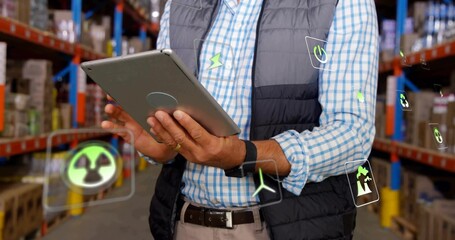Business casual supervisor monitoring tablet in warehouse aisle with boxes, floating energy icons