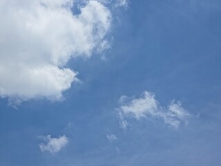 Clear blue sky with scattered white clouds, featuring larger clouds on the left and open blue space on the right, conveying a calm, sunny day.