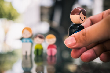Hand picking one wooden figure away from a group symbolizes divorce, separation, broken family,...