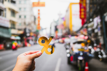 Hand holding a golden percent symbol on an empty street in Chinatown, symbolizing economic slowdown, low tourism, declining spending, inflation, interest rate, and financial recession in Thailand.