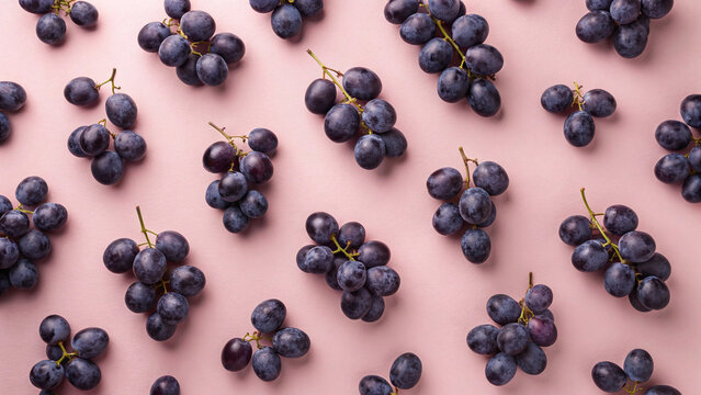 Fresh purple grapes arranged in a pattern on a pink background