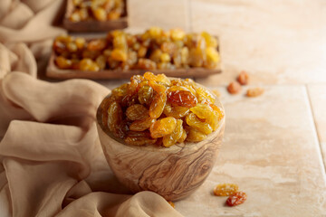 Yellow sultana raisins in a wooden bowl on a beige background.