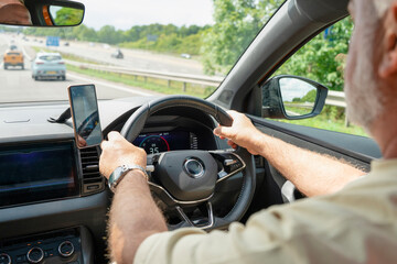 Driving on a sunny day with the hands on the steering wheel and mobile phone mounted for navigation and updates on a highway in the countryside