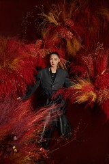 Woman in a black suit surrounded by vibrant red foliage in a modern art setting.