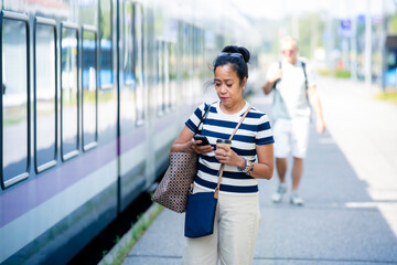 Confident Asian woman on train platform using smartphone, symbolizing modern city lifestyle, mobility, technology, commuting, and connectivity.