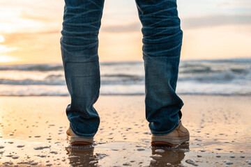 Person standing on the beach during sunset, waves gently lapping at their feet, creating a serene atmosphere and capturing a moment of reflection