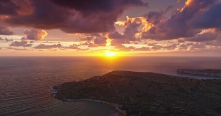 Malta: beautiful sunset over Mediterranean Sea with colorful clouds illuminating the rocky coast of Gozo, under bright sky, creating a breathtaking natural spectacle. Aerial view drone footage - Powered by Adobe