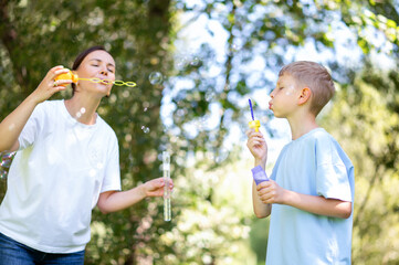 Fototapeta premium Blowing soap bubbles together: mother and teenage boy in park
