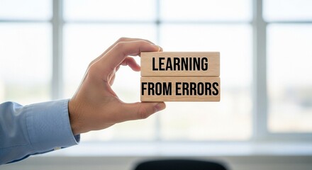 Hand holding wooden blocks displaying "Learning From Errors" - a powerful concept for personal and professional development