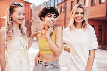 Three young beautiful smiling hipster female in trendy summer stylish clothes. Sexy carefree women posing in the street. Positive models having fun, hugging and going crazy, near brick wall