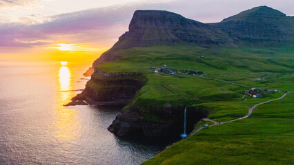 Captivating sunset light illuminates Mulafossur waterfall cascading into the Atlantic Ocean, near...