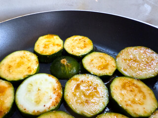 Fried zucchini slices with oil in pan, close up view, golden brown vegetable cooking on stove, healthy vegetarian or vegan meal preparation.