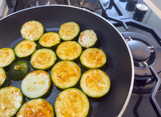 Sliced zucchini with seasoning frying in pan on stove, top view, fresh vegetable cooking process for healthy meal, vegetarian or vegan food preparation.