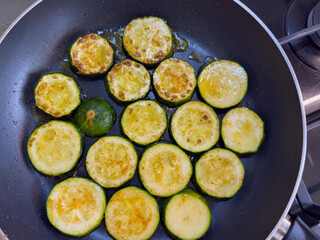 Fried zucchini slices with oil in pan, close up view, golden brown vegetable cooking on stove, healthy vegetarian or vegan meal preparation.