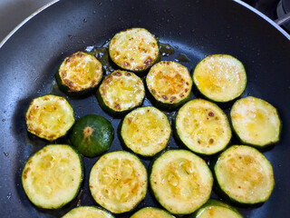 Fried zucchini slices with oil in pan, close up view, golden brown vegetable cooking on stove, healthy vegetarian or vegan meal preparation.