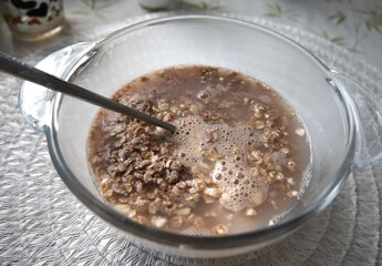 Creamy chocolate oatmeal served in a transparent glass bowl with a spoon, close-up view.