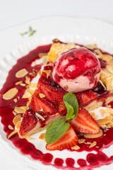 Close-up of a slice of strawberry pie served with a scoop of ice cream and almond flakes on a white background.