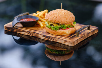 A freshly prepared cheeseburger served with crispy french fries and ketchup on a wooden serving...