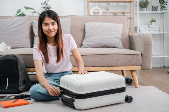 Smiling woman sitting on floor packing suitcase in living room, ready for travel or vacation. - Powered by Adobe
