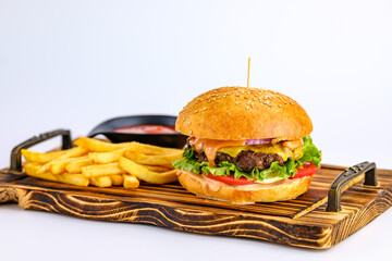A freshly prepared cheeseburger served with crispy french fries and ketchup on a wooden serving board