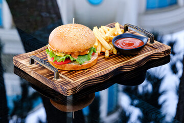 A freshly prepared cheeseburger served with crispy french fries and ketchup on a wooden serving...