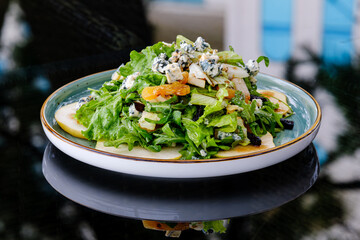 A vibrant green salad featuring fresh lettuce, sliced apples, blue cheese crumbles, and nuts, served on a ceramic plate