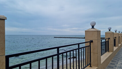 Seaside promenade with stone fence, metal railing, and lamps overlooking calm sea and cloudy sky