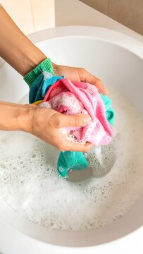 Hands washing colorful clothes in a sink filled with soapy water