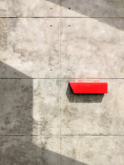 Red postbox on the old bare concrete wall in vintage loft style with sunlight and shadow on surface, front view and vertical frame