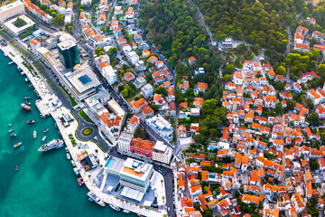 Drone top down photo of Split Riva promenade below Marjan Hill showing palm-lined waterfront, boats in the harbor, stone buildings and Adriatic coastline under summer skies
