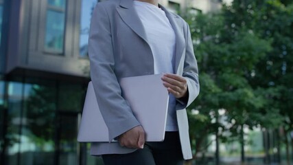 Confident businesswoman with laptop walking outside office