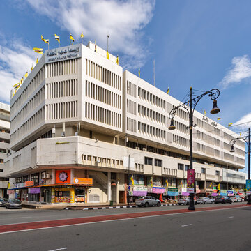 Bandar Seri Begawan, Brunei - Feb. 24, 2025: Wisma Hajjah Fatimah building. Urban street scene with shops, cars, and national flags under a blue sky