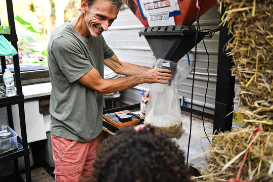 Man bags mushroom substrate while child watches on Florida farm