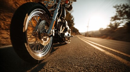 A low angle shot of a motorcycle on an asphalt road, trees on the sides, and bright sunlight in the distance, with a blurred background