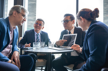 Obraz premium Asian businessman presenting work on laptop to group of businesspeople on table