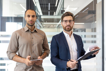 Two businessmen holding digital tablet and documents in office corridor