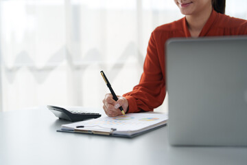 Businesswoman analyzing financial charts and taking notes in office