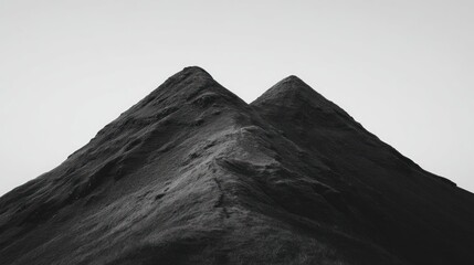 Two pointed mountain peaks ascend against a clear, pale sky, rendered in grayscale. The mountain face shows rugged texture and shadows