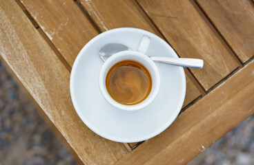 Hot espresso in a white cup and saucer on a wooden table in a beach restaurant. Morning black strong coffee