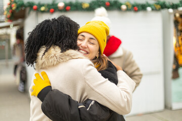 Two happy women hugging at christmas market, sharing a moment of joy and affection