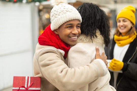 Friends exchanging christmas gift and hugging at market