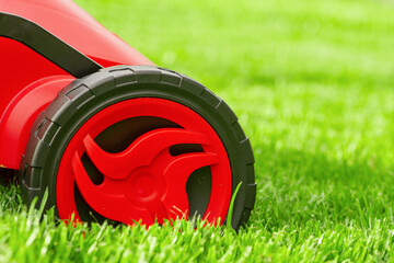 A close-up of a black and red lawn mower mowing on a green lawn.