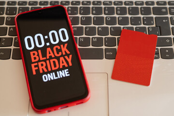 Red smartphone displaying black friday online countdown with 00:00 time and red credit card lying on laptop keyboard suggesting last-minute online shopping