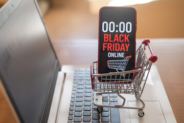 Shopping cart with smartphone showing black friday online countdown placed on laptop keyboard represents online shopping and discounts during black friday sales