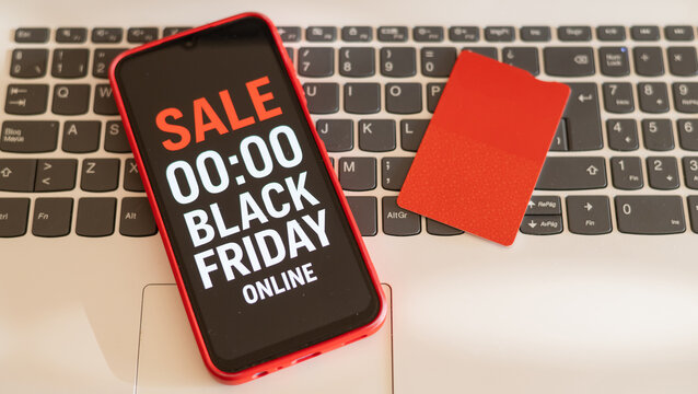 Red smartphone displaying black friday online sale countdown and red credit card lying on laptop keyboard suggest exciting shopping opportunities