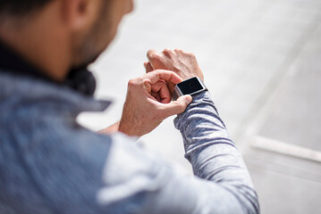 Man in sportswear checking smartwatch during running break in city
