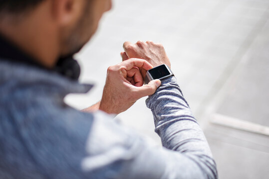 Man in sportswear checking smartwatch during running break in city