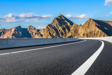 Asphalt highway road curves through a majestic mountain landscape with rugged rocky peaks under a beautiful blue sky