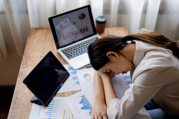 Overworked young businesswoman sleeping at office desk with laptop, symbolizing exhaustion, stress, deadlines, workplace challenges, and modern professional lifestyle.
